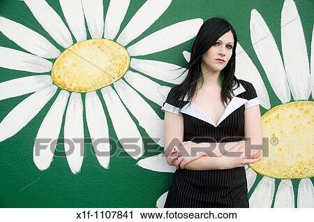 Stock Image - an attractive teenage girl with long black hair stabding against a wall with flowers painted on it. Fotosearch