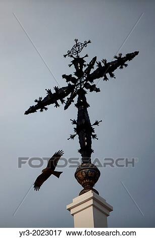 Stock Photo - An eagle flies near the cross of the Hermitage of the Virgin of Rocio, in Almonte, Donana National Park, Huelva province, Andalusia, Spain. Fotosearch