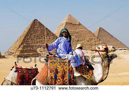 Stock Image - An Egyptian man and his camel asking tourist to come for a ride around the great Pyramids of Giza, Egypt.. Fotosearch