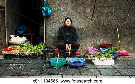 Stock Photography - An elderly Chinese woman sells vegetables in a street market at central Guilin, south China.. Fotosearch