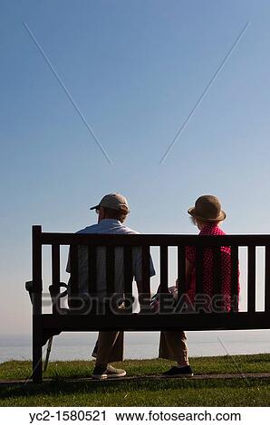 Stock Image - An elderly couple sit on a seaside bench looking out to sea in Southwold, Suffolk, England, Britain, Uk. Fotosearch