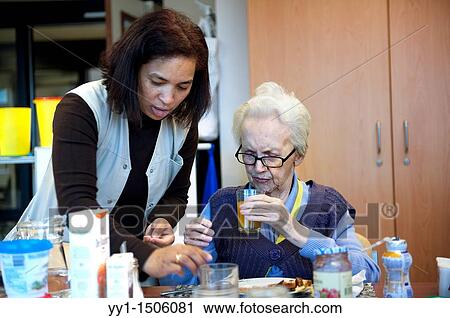 An elderly resident of a nursing home having breakfast at the communal breakfast table, while being helped out by a nurse. View Large Photo Image Stock Image - An elderly resident of a nursing home having breakfast at the communal breakfast table, while being helped out by a nurse.. Fotosearch