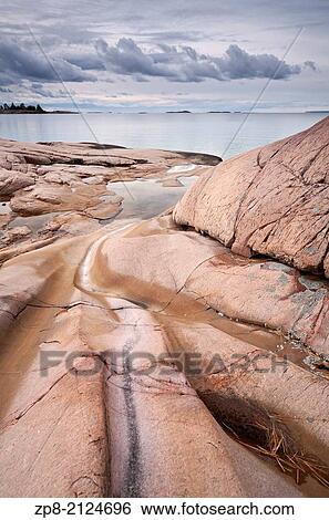 Stock Photograph - An example of rock being eroded by water and ice with dramatic storm clouds over Georgian Bay, Killarney Provincial Park, Ontario, Canada.. Fotosearch