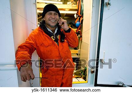 Stock Photograph - An Indonesian seaman or sailor on the container-vessel MV Flintercape, during a journey from Rotterdam, Netherlands, to Sundsvall, Sweden. The man is an? Able Seaman?, who generally works on deck, and now checks is phone near the tools-room on the deck.. Fotosearch