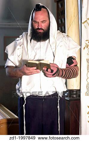 An Israeli Jewish orthodox man prays in a synagogue, reads a torah book (siddur) and wears, tefillin, tzitzit and tallit. View Large Photo Image Stock Photo - An Israeli Jewish orthodox man prays in a synagogue, reads a torah book (siddur) and wears, tefillin, tzitzit and tallit.. Fotosearch