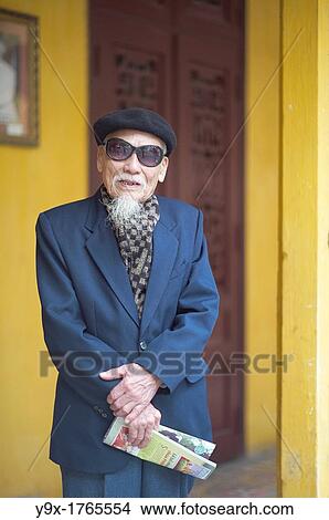 Picture - An old man in a blue suit, wearing an artist hat and sunglasses at a temple in Vietnam. Fotosearch