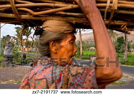Stock Photo - An old woman collects firewood along the road leading to the fishing village of Amed East Bali.. Fotosearch