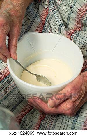 Stock Photo - An old woman stirring homemade icing in a bowl on her lap. Fotosearch