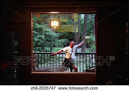 Stock Photo - An older asian man performing silly martial arts moves in front of a window with a forest behind him in Yosemite National Park.. Fotosearch