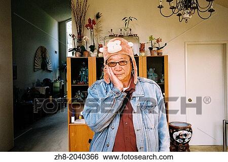 An older Asian man wears a monkey hat while holding his hand on his cheeks in the living room of his Californian home. View Large Photo Image Stock Photograph - An older Asian man wears a monkey hat while holding his hand on his cheeks in the living room of his Californian home.. Fotosearch