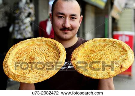 Stock Image - An Uighur man holding traditional Nan bread.. Fotosearch