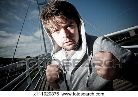 Angry aggressive young man with fists clenched wearing hooded hoodie top View Large Photo Image Stock Photograph - Angry aggressive young man with fists clenched wearing hooded hoodie top. Fotosearch