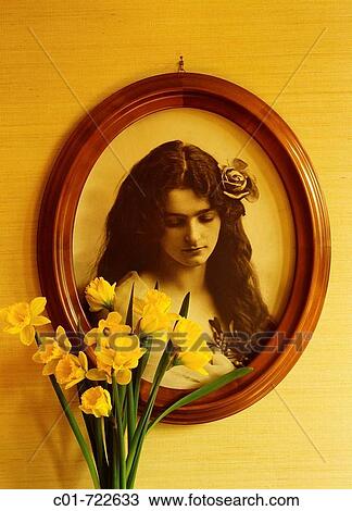 Stock Image - Antique photo of a long-haired woman (1920? s) in oval frame and daffodil flowers. Fotosearch