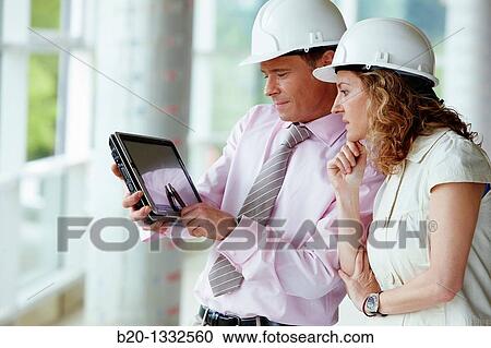 Stock Image - Architect and client with tablet PC in construction site. Fotosearch