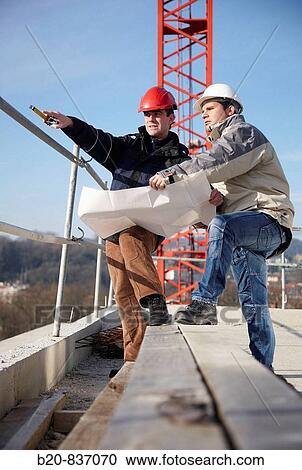 Stock Image - Architect and construction worker looking at blueprints, personal protective equipment, housing construction. Fotosearch