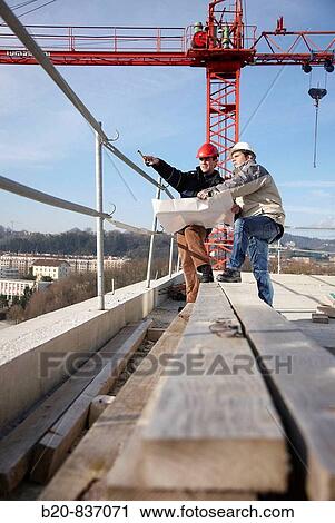 Stock Image - Architect and construction worker looking at blueprints, personal protective equipment, housing construction. Fotosearch