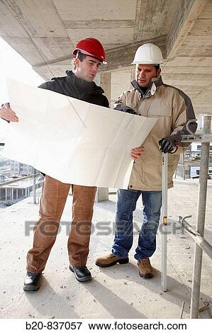 Stock Photo - Architect and construction worker looking at blueprints, personal protective equipment, housing construction, concrete skeleton. Fotosearch