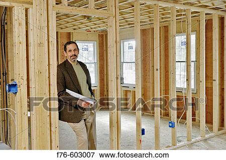 Stock Photo - Architect holding plans in partially constructed building,. Fotosearch