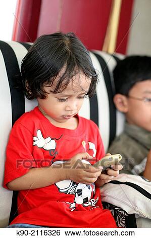 Stock Photograph - Asian boy playing with a smartphone, Jakarta, Indonesia, Southeast Asia.. Fotosearch