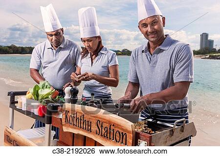 Stock Photograph - Asian catering chefs at the beach cooking with a Koththu station. Gold Coast, Queensland, Australia.. Fotosearch