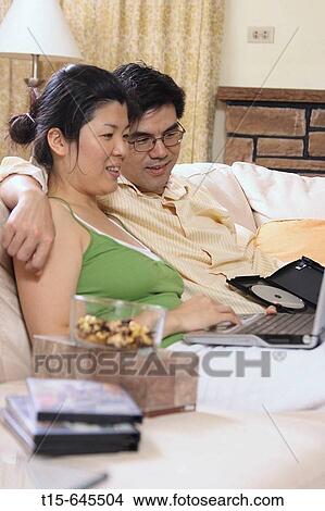 Picture - Asian couple in their 30's watching movie on laptop together happily. Fotosearch