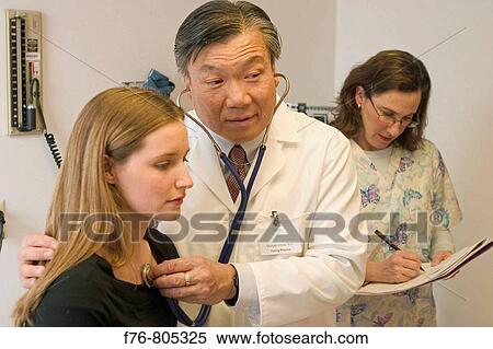 Asian doctor, listening to chest sounds of female patient, with stethoscope, in exam room of medical office with nurse, taking notes View Large Photo Image Stock Photography - Asian doctor, listening to chest sounds of female patient, with stethoscope, in exam room of medical office with nurse, taking notes. Fotosearch