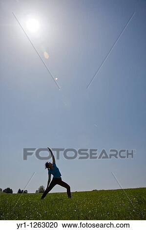 Stock Image - Asian girl doing yoga workout on a field during summer. Shot in Aachen, Germany.. Fotosearch