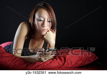 Asian girl in bed playing with iphone View Large Photo Image Stock Image - Asian girl in bed playing with iphone. Fotosearch