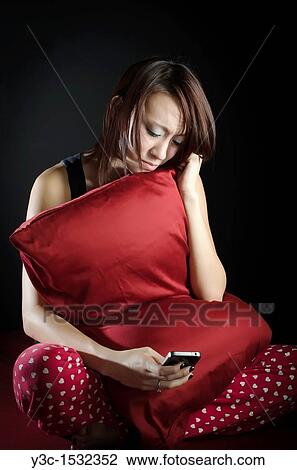Stock Image - Asian girl in bed playing with iphone. Fotosearch