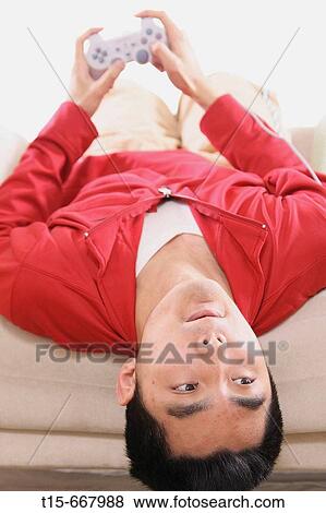 Asian man in his 20's playing video playstation game upside down on sofa View Large Photo Image Stock Photo - Asian man in his 20's playing video playstation game upside down on sofa. Fotosearch