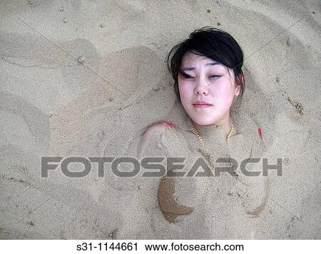 Stock Image - asian woman buried in sand on a beach. Fotosearch