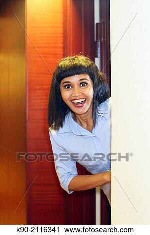 Stock Image - Asian woman looking out of the door around the corner, Jakarta, Indonesia, Southeast Asia.. Fotosearch