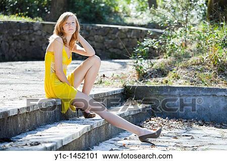 Stock Image - Attractive and slender young woman model is sitting in the park. Fotosearch