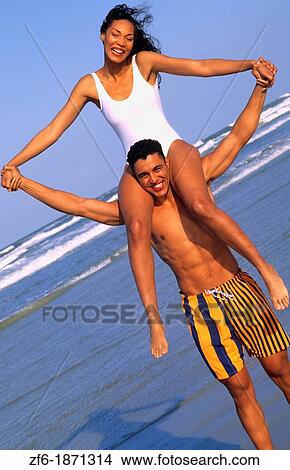 Attractive black african american couple in swim suits relaxing on the beach on holiday and enjoying the togetherness and caring View Large Photo Image Picture - Attractive black african american couple in swim suits relaxing on the beach on holiday and enjoying the togetherness and caring. Fotosearch