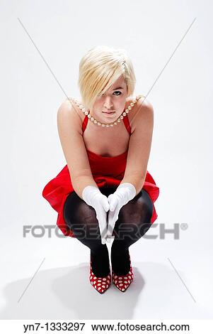 Attractive blond model in chirpy red and black outfit with large string of pearls sauatting down facing the camera View Large Photo Image Stock Photo - Attractive blond model in chirpy red and black outfit with large string of pearls sauatting down facing the camera. Fotosearch