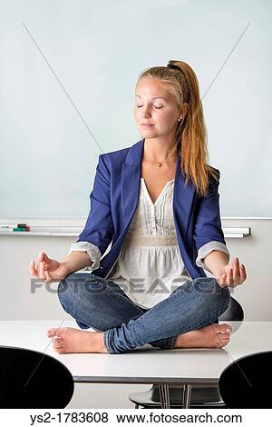 Attractive businesswoman sitting barefoot in yoga position on a table in her workplace View Large Photo Image Stock Photo - Attractive businesswoman sitting barefoot in yoga position on a table in her workplace. Fotosearch