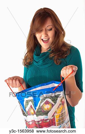 Attractive woman looks happily surprised while looking into Christmas themed shopping bag View Large Photo Image Stock Photo - Attractive woman looks happily surprised while looking into Christmas themed shopping bag. Fotosearch