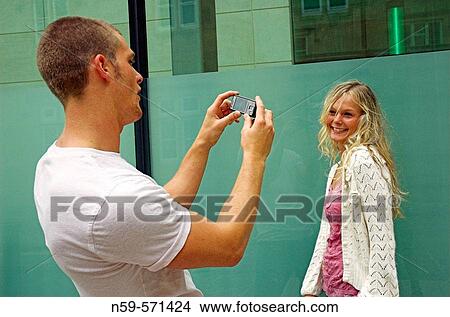 Attractive young couple playing with a cell phone camera. The boyfriend is photographing his girlfriend. View Large Photo Image Picture - Attractive young couple playing with a cell phone camera. The boyfriend is photographing his girlfriend.. Fotosearch