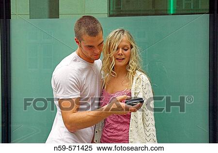 Attractive young couple playing with a cell phone camera. The boyfriend is showing his girlfriend pictures. View Large Photo Image Stock Photography - Attractive young couple playing with a cell phone camera. The boyfriend is showing his girlfriend pictures.. Fotosearch