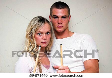 Stock Image - Attractive young couple pose with pool cues.. Fotosearch