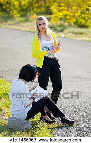 Stock Image - Attractive young female students together by the country-road and waiting. Fotosearch