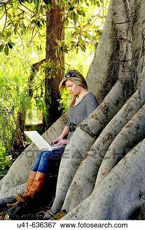 Attractive young female working on her computer while sitting in an old tree in the garden View Large Photo Image Stock Photo - Attractive young female working on her computer while sitting in an old tree in the garden. Fotosearch