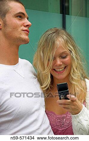 Attractive young urban couple, looking at messages on mobile phone. View Large Photo Image Picture - Attractive young urban couple, looking at messages on mobile phone.. Fotosearch