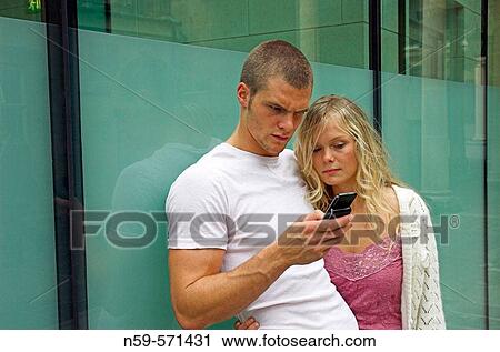 Attractive young urban couple, looking at messages on mobile phone. View Large Photo Image Stock Image - Attractive young urban couple, looking at messages on mobile phone.. Fotosearch