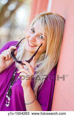 Stock Image - Attractive young woman happy and smiling with sunglasses in hands. Fotosearch