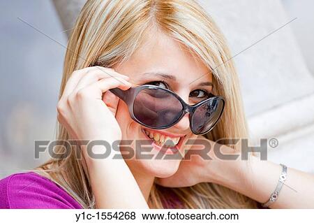Stock Photo - Attractive young woman happy and smiling looking over sunglasses. Fotosearch