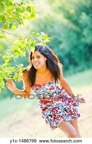 Stock Photo - Attractive young woman happy behind a tree branch. Fotosearch