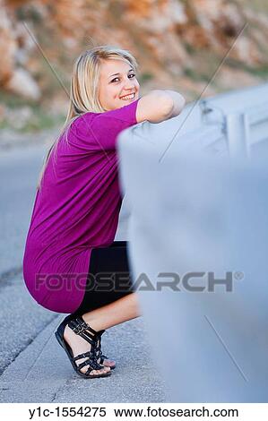 Stock Photography - Attractive young woman happy smiling smile squatting by the road. Fotosearch