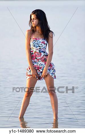 Stock Image - Attractive young woman hiking up her Summer dress exposing legs. Fotosearch