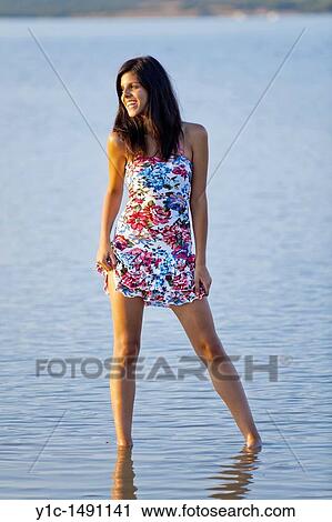 Stock Image - Attractive young woman hiking up her Summer dress exposing her thigh. Fotosearch